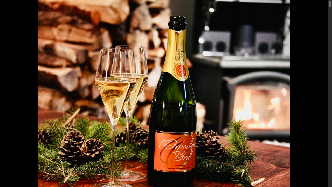 Vin pétillant l'Orpailleur Brut, avec verres flûtes et branches de sapin devant un poêle à bois